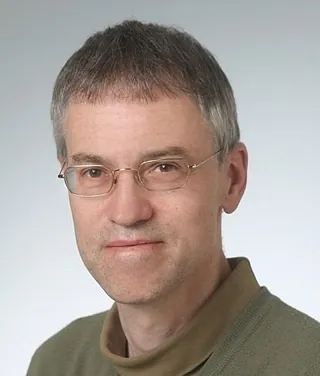 Mann mit Brille, kurzen grauen Haaren, grüner Pullover.