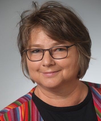 Lächelnde Frau mit Brille und bunter gestreifter Jacke.